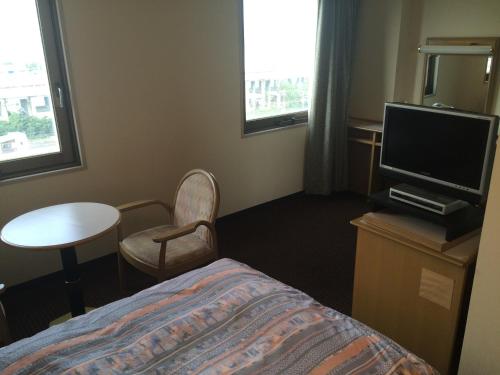 a hotel room with a bed and a tv and a table at Hotel Crown Hills Tokuyama in Shunan