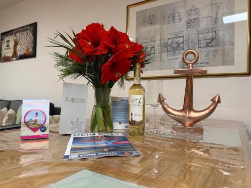 a table with a vase of red flowers and a bottle of wine at Sylter Seestern App Ankerplatz in Morsum