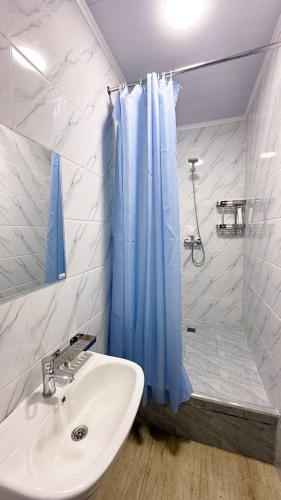 een badkamer met een wastafel en een douche met een blauw douchegordijn bij Ugolok Xostel in Yakkasaray