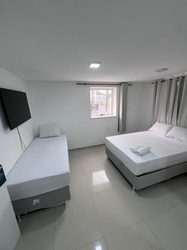 a white room with two beds and a tv at Pousada Pergentino in Maceió