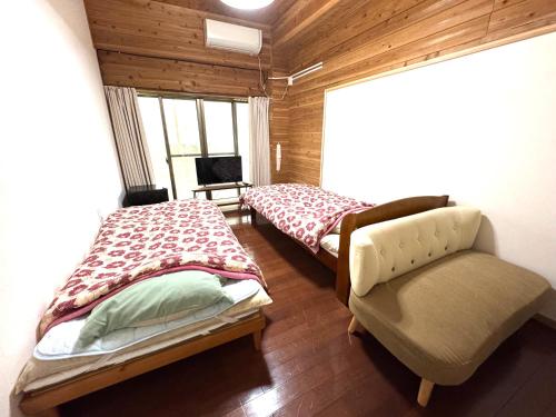 a room with two beds and a chair and a window at 徳之島体験お宿結屋 in Inokawa