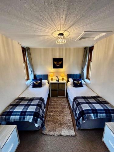two beds in a room with a chandelier at Shetland Cottage Kincraig in Kincraig