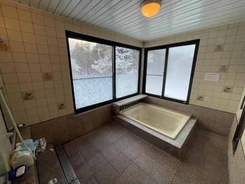 un bagno con vasca e 2 finestre di ペンション歩野慕野-honobono a Kitashiobara