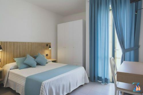 een slaapkamer met een bed met blauwe gordijnen en een bureau bij Zeeva Hotel and Resort in Torre Dei Corsari