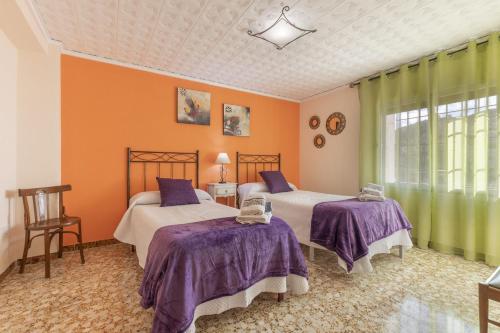 2 Betten in einem Zimmer mit orangefarbenen Wänden und lila Bettwäsche in der Unterkunft La Herreria de Esteban in Cuevas Labradas