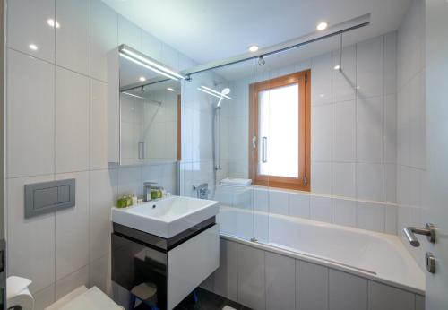 a white bathroom with a sink and a bath tub at Chalet Waldschluecht in Wengen