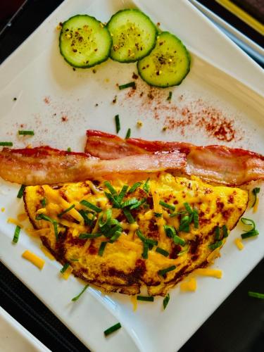 a plate with an omelet with bacon sausage and cucumbers at Sawubona Guesthouse in Beach View