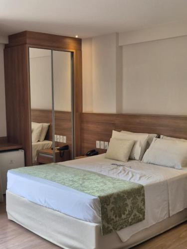 a bedroom with a large white bed with a mirror at Vista Azul Apart Hotel - Vista Pinheiros in Pedra Azul