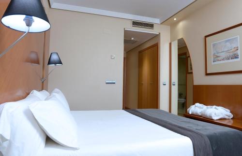 a bedroom with a large white bed and a lamp at Silken Juan de Austria in Valladolid