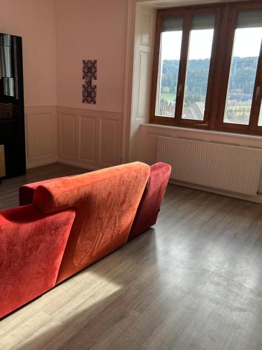 een rode bank in een woonkamer met ramen bij Le séjour in Tramelan