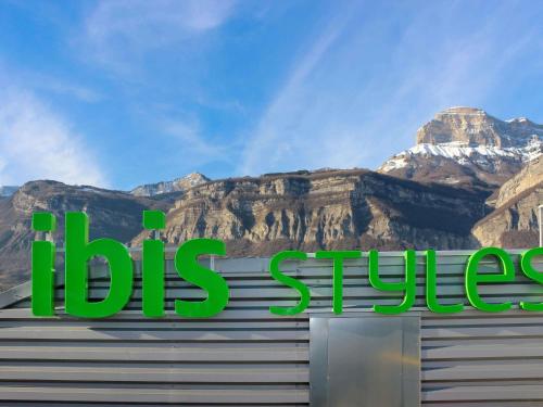 a sign on top of a building with mountains in the background at Ibis Styles Crolles Grenoble A41 in Crolles