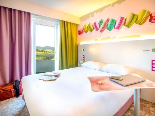 ibis Styles Fréjus St Raphael في فريجوس: غرفة نوم مع سرير أبيض مع جهاز كمبيوتر محمول على طاولة