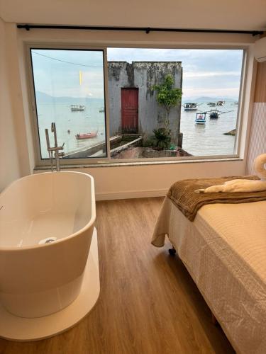 a bathroom with a tub and a bed and a window at Morada Som do Mar in Governador Celso Ramos