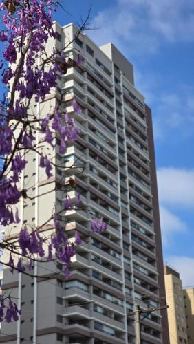 Un palazzo alto con fiori viola davanti di Dani Studio Moema Grand Vitrali a San Paolo