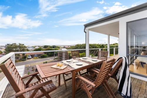 a deck with a wooden table and chairs on a balcony at Hazel Beach House - Ocean Views & Coastal Charm in Goolwa South