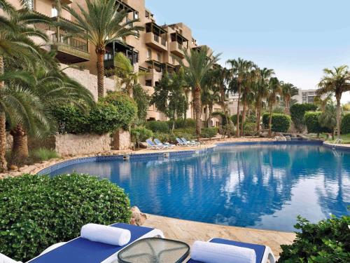 a large swimming pool with lounge chairs and palm trees at Mövenpick Resort & Residences Aqaba in Aqaba