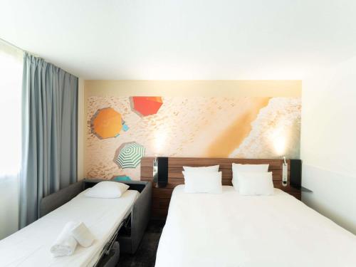 2 bedden in een hotelkamer met witte kussens bij Novotel Antibes Sophia Antipolis in Valbonne