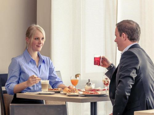 Ein Mann und eine Frau sitzen an einem Tisch und essen in der Unterkunft Fürther Hotel Mercure Nürnberg West in Fürth