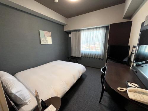 a hotel room with a bed and a desk with a phone at Hotel Route-Inn Sakaide-Kita Inter in Sakaide