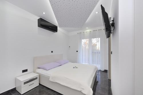 a white bedroom with a bed and a tv at Villa Lily in Privlaka