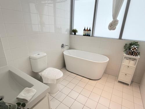 a white bathroom with a tub and a toilet at Burwood Luxe Urban Escape in Sydney