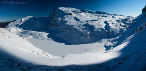 a mountain covered in snow with a blue sky at Papaevangelou Hotel in Papigko
