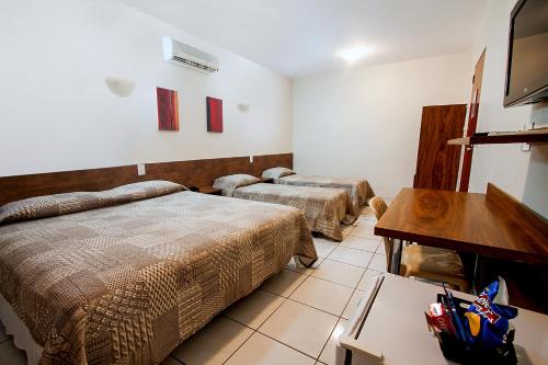 Habitación con 2 camas, mesa y TV. en Hotel Maraja en Uberlândia