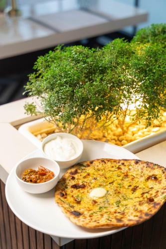 Eine Pizza auf einem Teller mit zwei Schüsseln mit Dips. in der Unterkunft The Madelinne Hotel in Muzaffarnagar