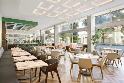 a restaurant with white tables and chairs and windows at Carte Hotel San Diego Downtown, Curio Collection By Hilton in San Diego