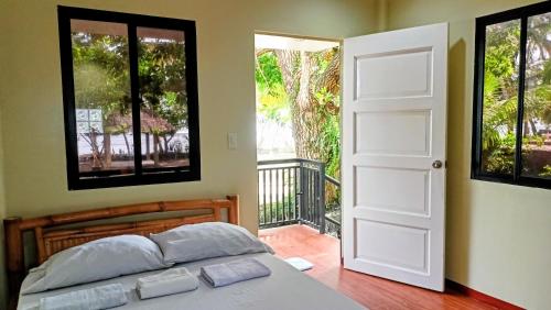 a bedroom with a bed and a door to a balcony at Suki Beach Resort Beachfront Cottage in Santa Magdalena