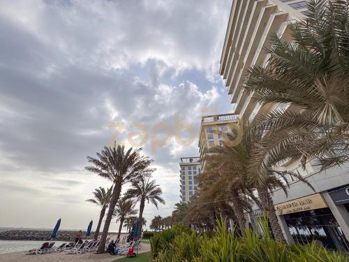 a building on the beach with palm trees and a building at ZAPBED HOUSE -1 BR In Pacific Tower Al Marjan Island With Beach Access Ras Al Khaimah in Ras al Khaimah
