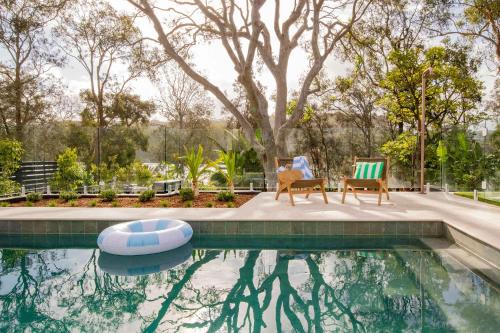 two chairs and a swimming pool with trees in the background at Surf Lodge Avoca Beach Waterfront to Avoca Lake in Avoca Beach