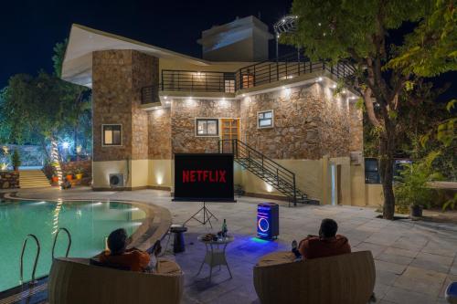 two people sitting in chairs by a swimming pool at night at SaffronStays Grand Pavilion in Udaipur