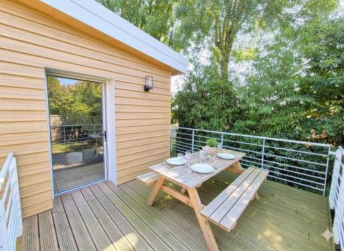 a wooden picnic table on a deck with a sliding glass door at Cottage Les Ormeaux - à 13 minutes du Puy du Fou in Les Herbiers
