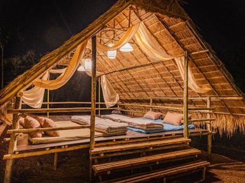un lit dans une hutte de paille avec des oreillers dessus dans l'établissement Ozone Valley Camp Khaoyai, à Nong Nam Daeng