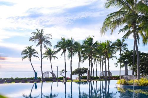 a pool with palm trees and the ocean in the background at Sheraton Hua Hin Resort & Spa in Cha Am