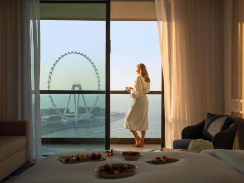 une femme debout devant une fenêtre dans une chambre d'hôtel dans l'établissement Sofitel Dubai Jumeirah Beach, à Dubaï