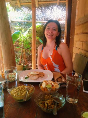 迪克韦勒Lunuvila Resort Hiriketiya Dikwella的一位女士坐在桌边，面前摆着一盘食物