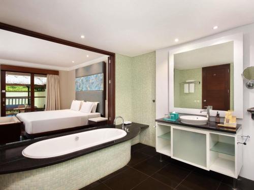 a bathroom with a bed and a tub and a sink at Novotel Bali Nusa Dua in Nusa Dua