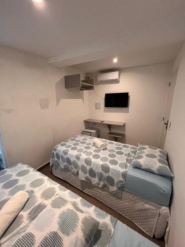 two beds in a small room with a tv at Manaira Suite 03 com 2 camas de solteiro ou 1 de casal in João Pessoa