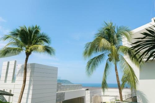 twee palmbomen naast een gebouw en de oceaan bij The Seaview Kata in Kata Beach