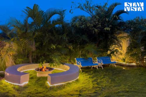 deux bancs bleus et un foyer dans une cour dans l'établissement StayVista at Thalassa Near The Beach, à Alibaug