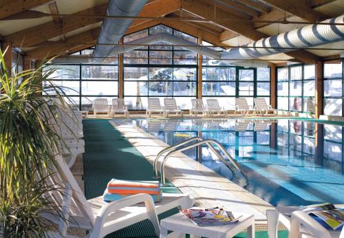 a large swimming pool with white chairs and tables at Camping L'Oustalet in Châtel