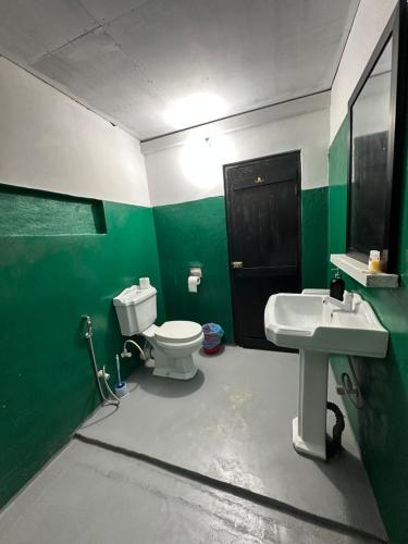 a green and white bathroom with a toilet and a sink at Seasong Rooms in Unawatuna