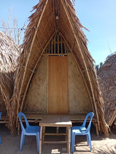 a thatched hut with two chairs and a table in front at El Hermosa Bice Camp in El Nido