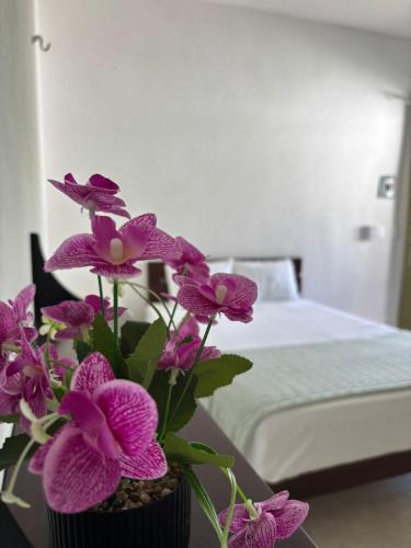 a vase with purple flowers on a table next to a bed at Casa Jatsutsil Bacalar in Bacalar
