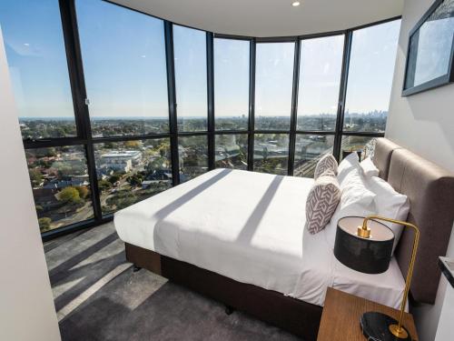 een slaapkamer met een bed in een kamer met hoge ramen bij The Sebel Melbourne Malvern in Melbourne