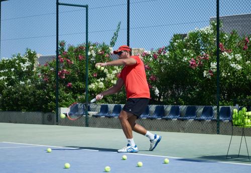 a man swinging a tennis racket on a tennis court at Ikaros Beach, Luxury Resort & Spa - Adults Only in Malia