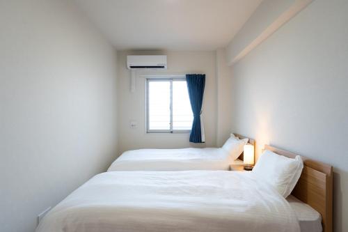 twee bedden in een kleine kamer met een raam bij KAI Okinawa in Kitanakagusuku