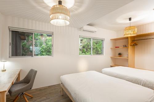 a bedroom with two beds and a desk and two windows at Lucia Seaside Villa Amami in Amami